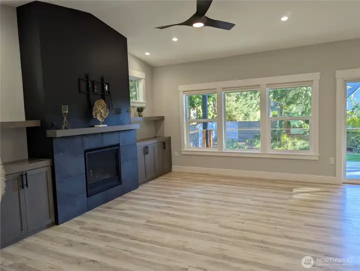 Open floor plan. Built-in cabinets and shelves, stacked stone propane fireplace, modern ceiling fan, luxury vinyl plank flooring