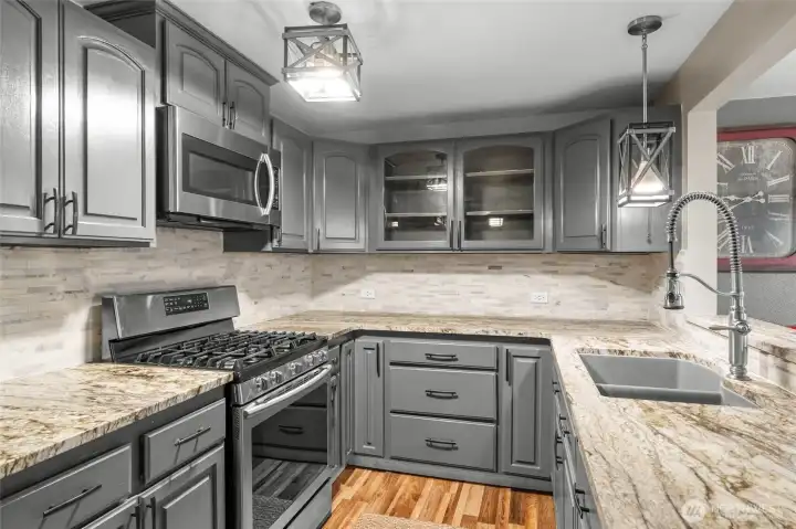 MAIN LEVEL | Just around the corner from the living room is the stunning kitchen with updated countertops, stainless steel appliances, gas range and modern lighting.