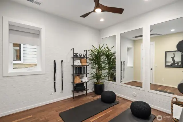 Main floor bedroom space with white brick tiled walls, custom wall mirrors & ceiling fan light fixture perfect as a private yoga fitness area
