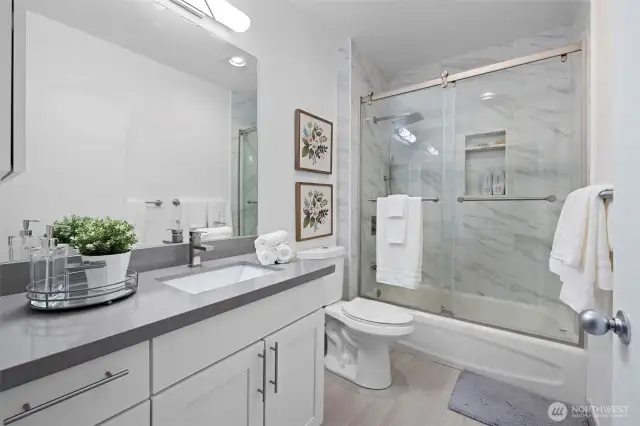 Newly updated bathroom with tile surround shower, quartz countertop, tile floor and white cabinets.