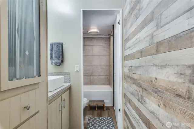 Entry to the primary bathroom features new LVP flooring, rustic accent walls and built-in linen storage.