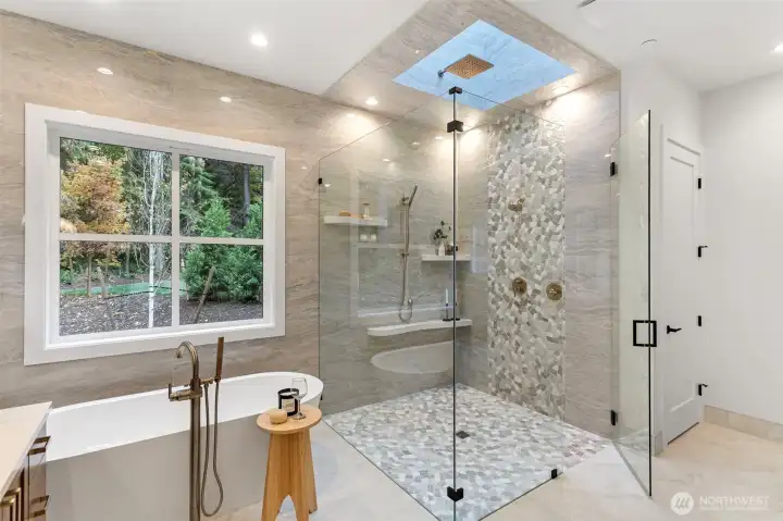 Spa-inspired primary bathroom featuring a standalone soaking tub, dual vanities, and a dedicated makeup desk. The custom shower is the showpiece—illuminated by a skylight above and enhanced with a ceiling-mounted rain head, creating a serene, light-filled retreat.