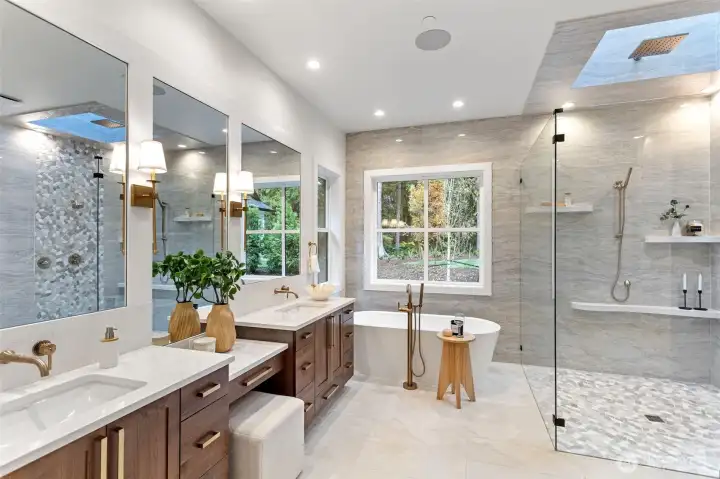 Elegant and serene, the primary bathroom showcases luxurious finishes and thoughtful design. Soft natural light filters through the skylight, highlighting the sleek quartz surfaces, designer fixtures, and custom cabinetry. Every element—from the freestanding tub to the expansive glass-enclosed shower—blends spa-level comfort with modern sophistication.