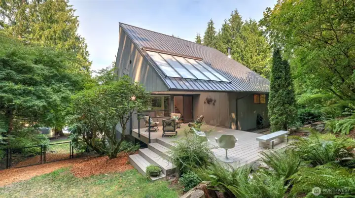 Enjoy this striking architectural design and low-maintenance metal roof surrounded by lush greenery, complete with a spacious deck for outdoor living.