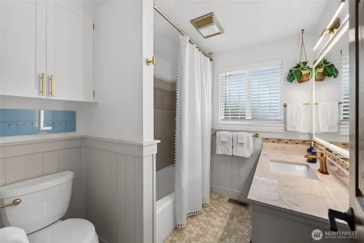 The newly refreshed full bath boasts a lighted hotel mirror, board & batten walls, honeycomb tile flooring and a beautiful vanity with engineered countertop and stylish gold tone fixtures.