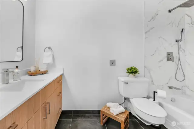 Primary suite bathroom features new vanity, quartz counter, tile floor, mirror, lighting, hardware and classy tile tub surround.