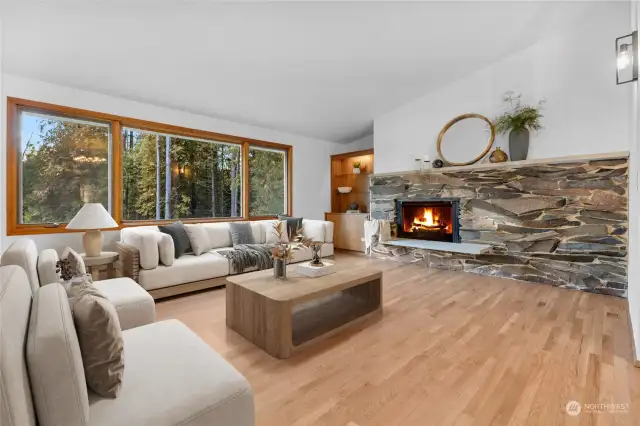 Spacious living room with wood-burning stone fireplace, wood-framed thermo-pane windows and refinished hardwood floors. (digitally staged)