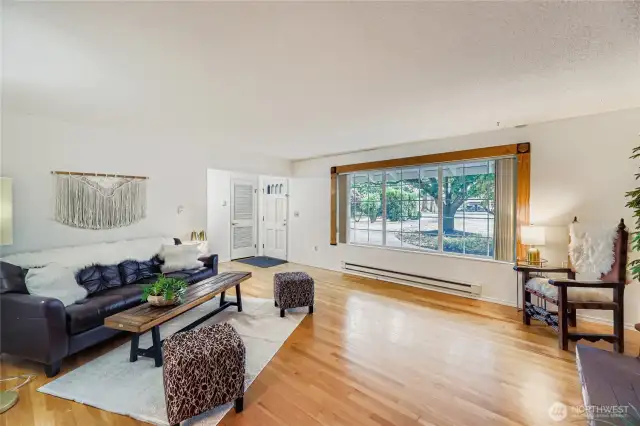 Bright and spacious living room with beautiful hardwood floors and a large picture window framing peaceful front yard views.