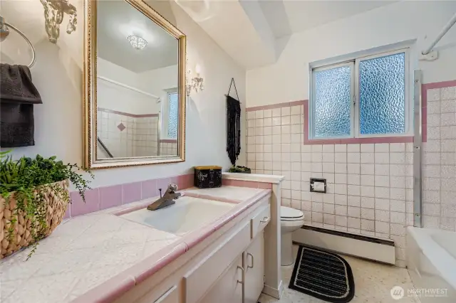 Retro-chic full bath with vintage pink tile, spacious vanity, and natural light from the window.