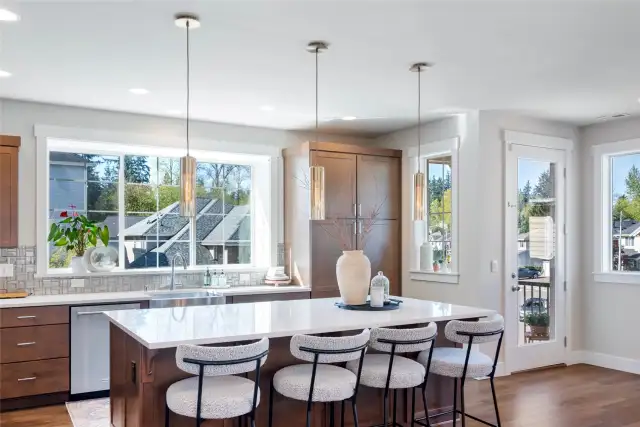 Chef-inspired kitchen with quartz countertops, a generous island, designer pendants, stainless steel appliances, rich cabinetry and a large window.