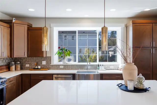 Chef-inspired kitchen with quartz countertops, a generous island, designer pendants, stainless steel appliances, rich cabinetry and a large window.