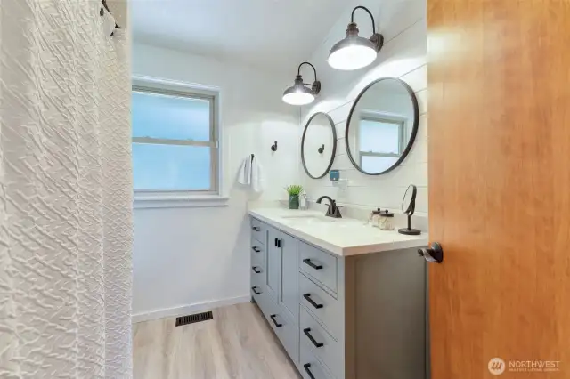 Upstairs bathroom with full tub/shower & new flooring, vanity, toilet, lighting & hardwood shiplap wall.