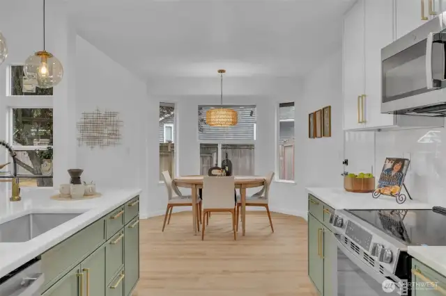 The chef's kitchen features on-trend sage green cabinetry with gold hardware and flows effortlessly into a sunny dining nook surrounded by windows. Multiple windows and thoughtful lighting create a bright, airy space perfect for both daily meals and entertaining.