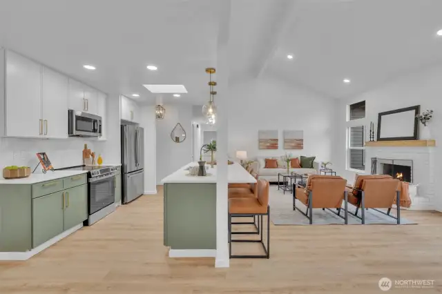 The open-concept design connects kitchen and living spaces under vaulted ceilings with a skylight that bathes the entire area in natural light. A cozy fireplace anchors the living room while the kitchen island provides a natural transition between spaces.
