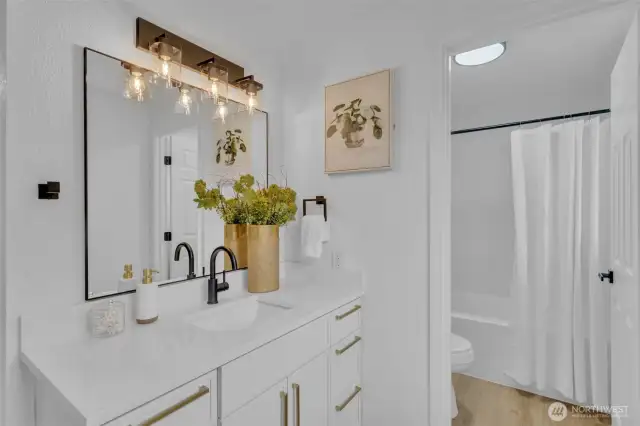 The primary en-suite bathroom features dual vanities with brass hardware, black fixtures, and a skylight that brightens the space.
