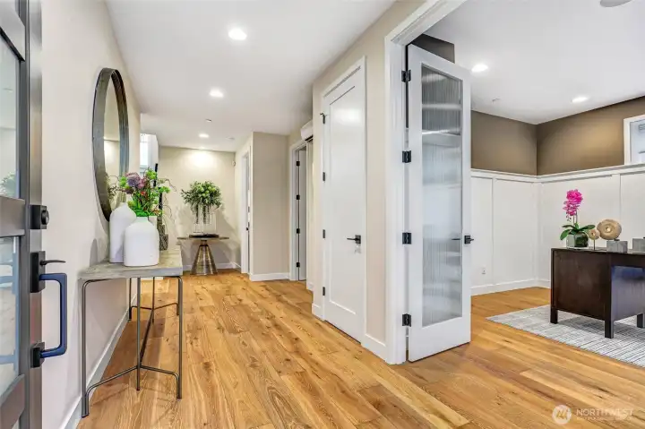Inviting entry hallway with wide-plank hardwoods and designer lighting. French doors open to a private main-level office with custom millwork and oversized windows that bring in natural light.