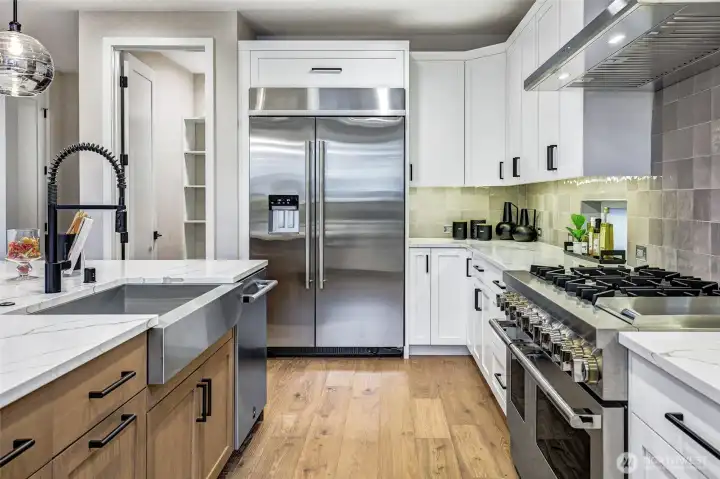 A chef-inspired kitchen anchored by a premium JennAir refrigerator and a 48-inch professional gas range. Expansive quartz surfaces, a deep stainless farmhouse sink, and curated pendant lighting combine to create a workspace that is both functional and beautifully designed. The walk-in pantry just beyond the refrigerator offers exceptional storage and organization.