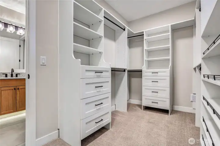 Spacious walk-in closet with custom built-ins, generous hanging space, and soft carpet underfoot — an organized dressing retreat right off the primary suite