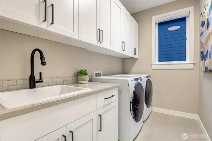 Bright and spacious laundry room featuring a deep utility sink, extensive cabinet storage, and modern front-load washer and dryer. Located near the upstairs bedrooms for everyday convenience.