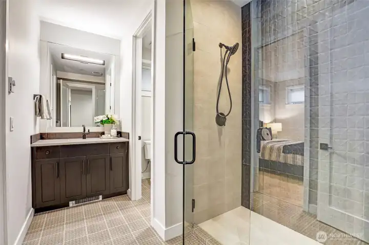 A beautifully appointed ensuite bath featuring a wide vanity, quartz counters, and striking matte-black fixtures. The oversized frameless glass shower showcases dimensional designer tile for a clean, modern finish, while thoughtful layout provides privacy and ease of use for adjacent bedroom with direct ensuite access.