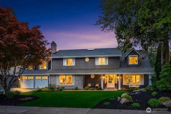 The home's exterior glows beautifully at dusk, with warm lighting highlighting the classic architecture, lush landscaping, and exceptional curb appeal that make this Buchan-built Timberline residence truly unforgettable.