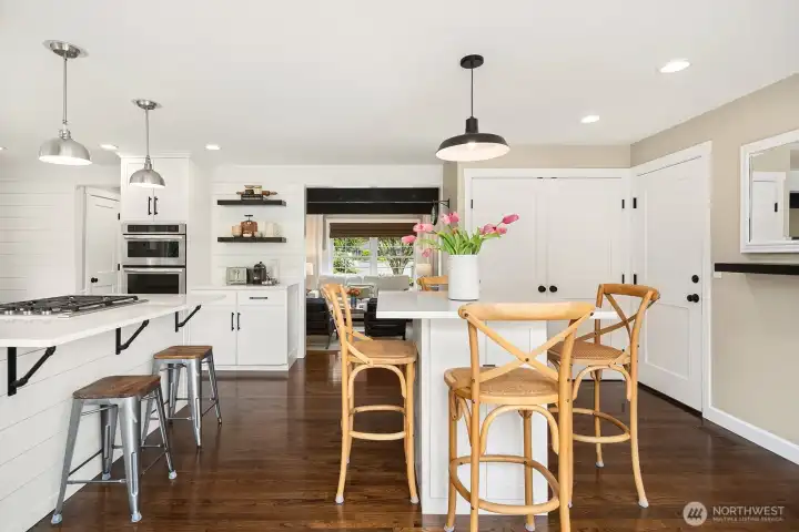 A wider view captures the effortless connection between the casual dining area and the kitchen, with rich hardwood floors, designer pendants, and an abundance of natural light tying the entire space together beautifully.