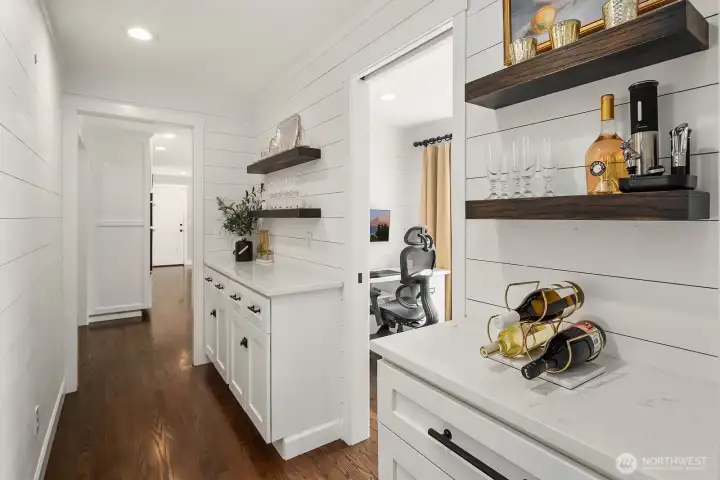 A thoughtfully designed butler's pantry or coffee bar area offers additional prep space and storage, seamlessly connecting the kitchen and dining areas with the same crisp white cabinetry and hardwood floors found throughout.