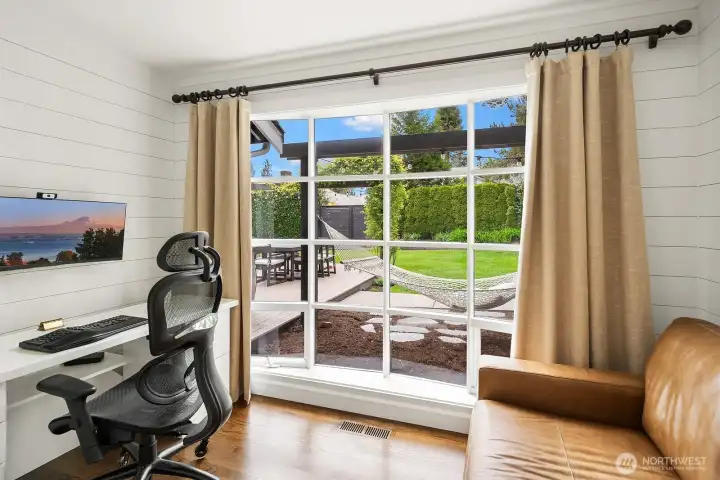 The sun-filled office overlooks the lush private backyard through large sliding glass doors, offering a peaceful and inspiring workspace with direct access to the beautifully landscaped outdoor retreat.