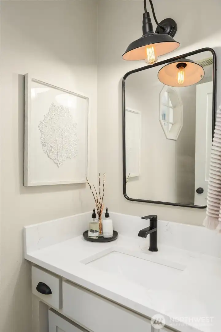 A beautifully appointed half bath features crisp white cabinetry, a sleek vanity, and stylish fixtures — a polished finishing touch that reflects the quality and attention to detail found throughout this immaculate home.