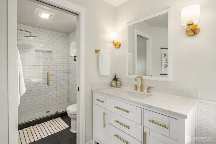 The primary bath's walk-in shower and additional vanity space complete this beautifully appointed suite, with crisp white finishes and warm brass fixtures lending a timeless, high-end feel.