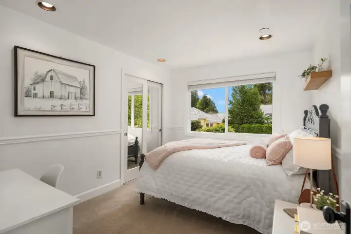 A bright and inviting secondary bedroom features a large window with lovely garden views, generous floor space, and the same warm, well-maintained finishes that define every room in this turnkey home.