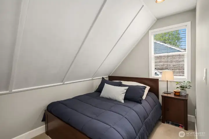 A charming third bedroom tucks under the roofline with architectural character, a bright window, and a cozy, intimate feel — a unique and delightful space that would make a perfect guest room or creative retreat.