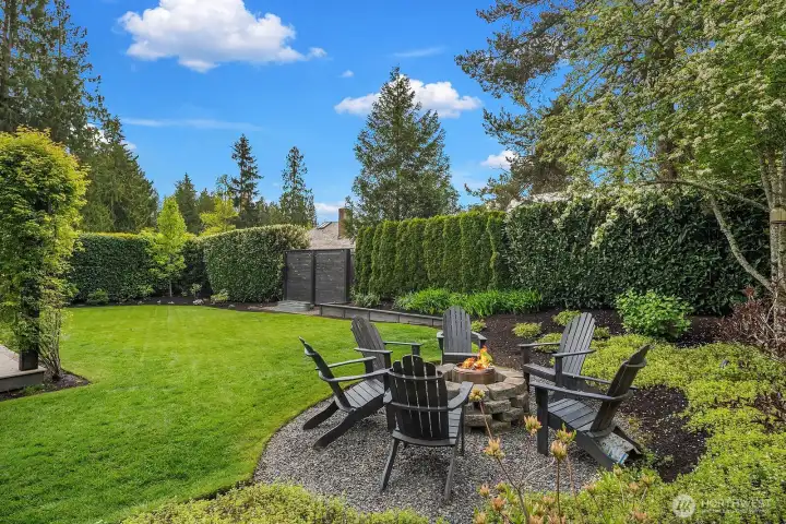 The backyard fire pit area invites year-round outdoor living, surrounded by mature privacy landscaping and a beautifully maintained lawn — a perfect setting for evening gatherings under the open sky.
