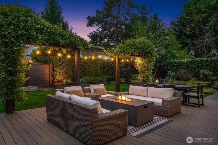 The Trex deck transforms into a magical evening retreat, with warm string lights casting a golden glow over the outdoor lounge and fire pit — proof that this backyard was made for year-round entertaining.