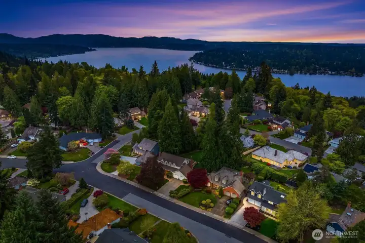 A stunning dusk aerial captures the home glowing warmly against the twilight sky, with the shimmering waters of Lake Washington visible in the distance — a breathtaking reminder of the unbeatable setting this Timberline neighborhood provides.
