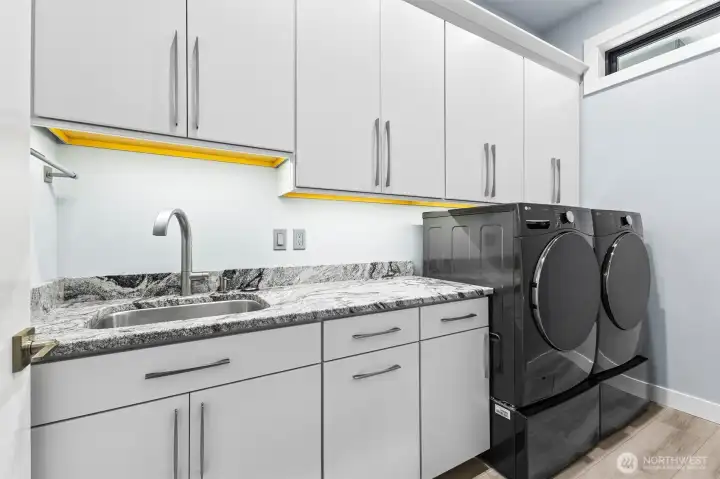 Main level laundry with granite surface finished with indirect lighting with front loader LG appliances, with under pedestal drawers.