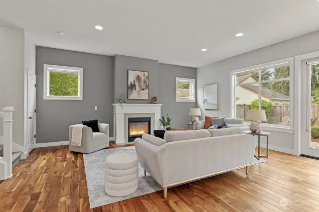 The living room is bright and spacious, outfitted with engineered hardwood floors, large windows and a cozy fireplace.