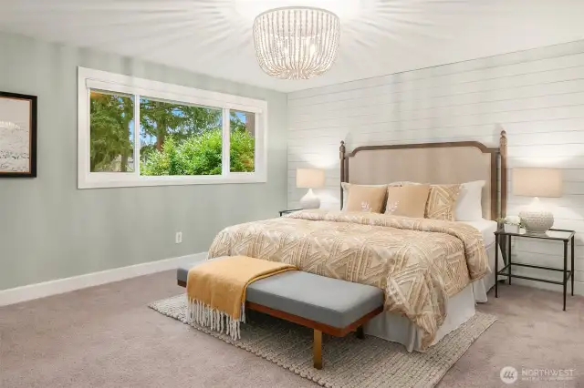 The roomy primary bedroom features a distinguished accent wall, soothing interiors and a wealth of natural light with serene views of the tree-laden back yard.