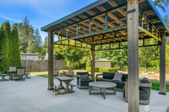 A beautiful and spacious outdoor gathering area with patio, pergola, firepit and plenty of grassy area for play.