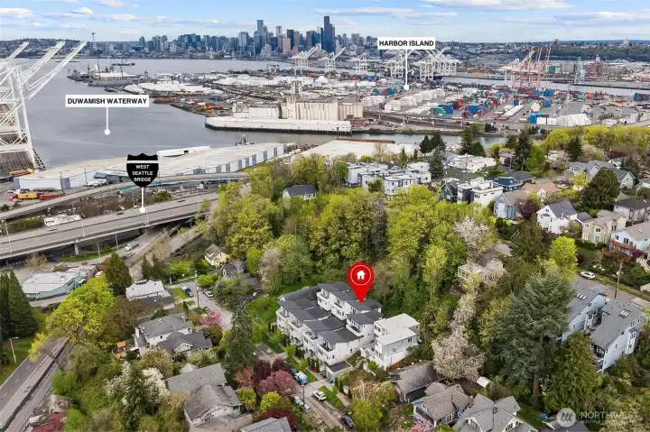 Elevated aerial perspective highlighting location between Pigeon Point hillside and the Duwamish Waterway with downtown Seattle skyline in the distance.