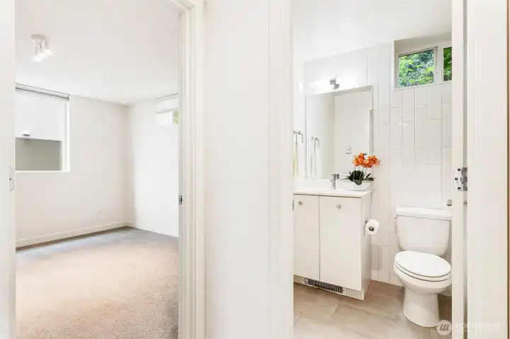 Lower level bedroom adjacent to full bathroom with vanity, tile flooring, and shower/tub combination.