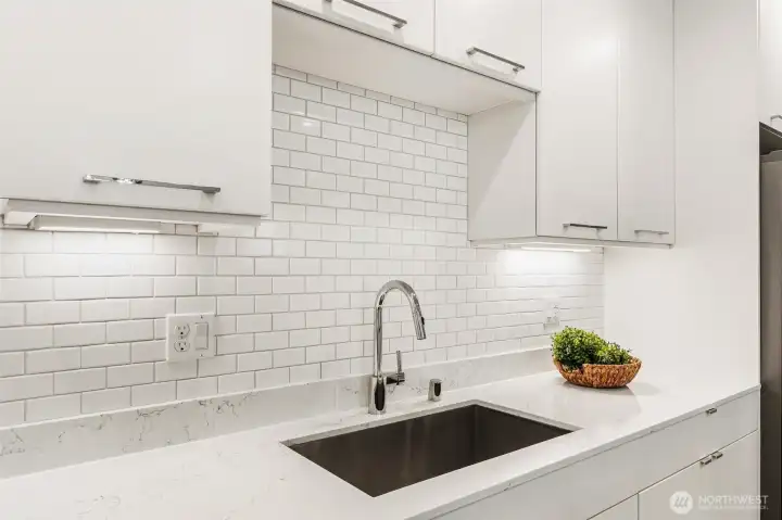 Kitchen detail with undermount sink, quartz counters, tile backsplash, and cabinet storage.