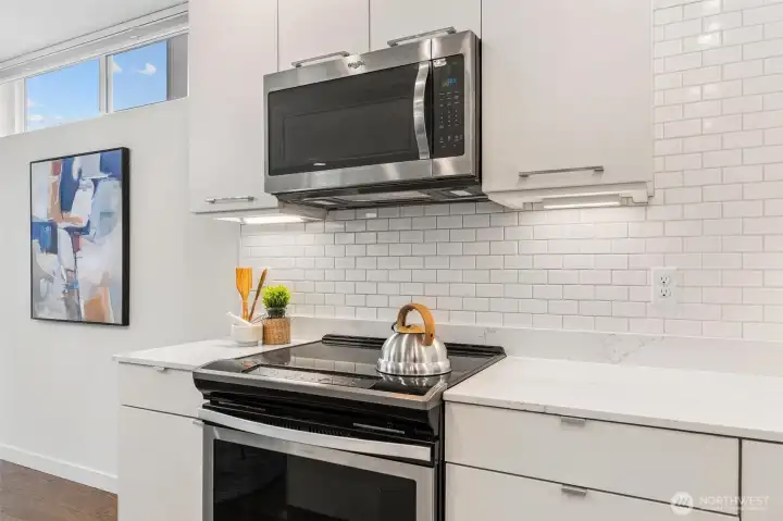 Kitchen appliance detail featuring stainless steel range, microwave, and tile backsplash.