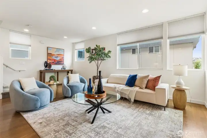 Living area with hardwood flooring, multiple windows for natural light, and open connection to kitchen and dining spaces.