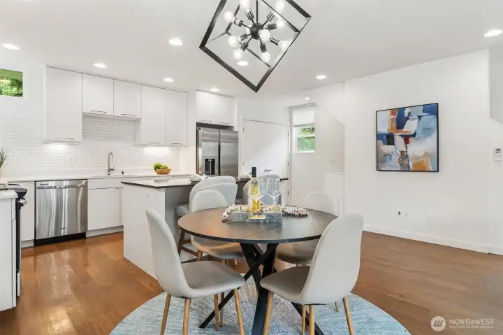 Dining area adjacent to kitchen with hardwood flooring, modern lighting, and open-concept layout.