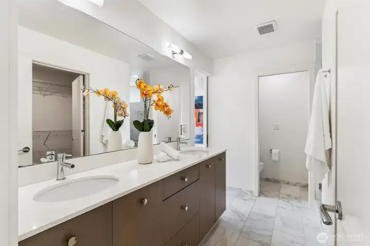 Primary bathroom with double vanity, solid surface counters, tile flooring, and walk-in closet access.