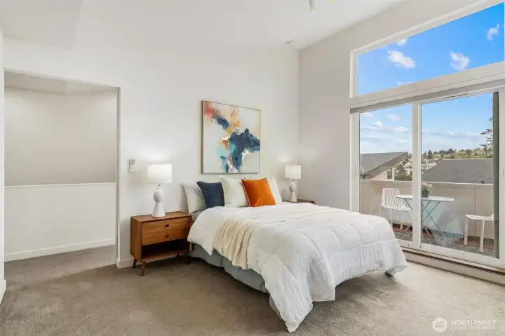 Primary bedroom with carpet flooring, vaulted ceiling, and sliding glass door to private deck.