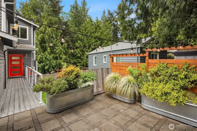 East-facing front yard patio framed by mature trees and a private metal gate offers a peaceful entrance.