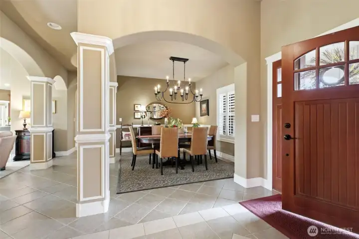Welcoming entryway with dramatic tray ceiling, warm cove lighting, elegant crown molding and arched openings.