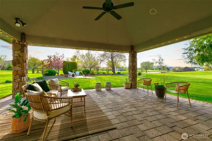 Covered patio with ceiling fan, brick pavers, built-in speakers, string lighting and stone columns.